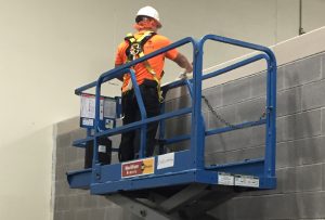 A man in safety orange uses a scissor lift. All part of industrial painting contractors normal routines.